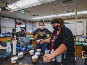 A faculty member and students in a lab looking at jars of different turf grasses and soils