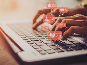 Hands on a keyboard with social media likes, shares, comment bubbles
