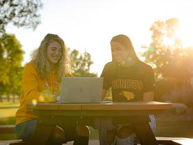 Two students early in the morning sitting at a table on the Campus Mall with their laptops