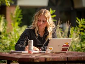 Female student working on a laptop outside at a picnic table on-campus