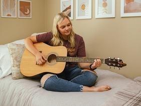 Female student playing a guitar on her bed in Centennial Hall