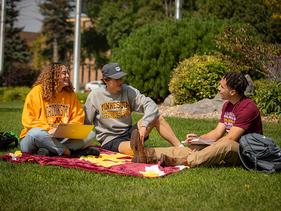 Three students sitting on a blanket on the Campus Mall in the summer